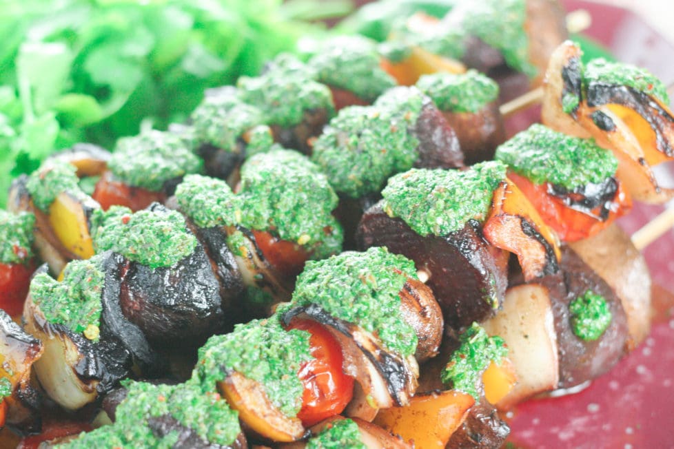 A close up of a plate of veggie skewers with basil chimichurri sauce