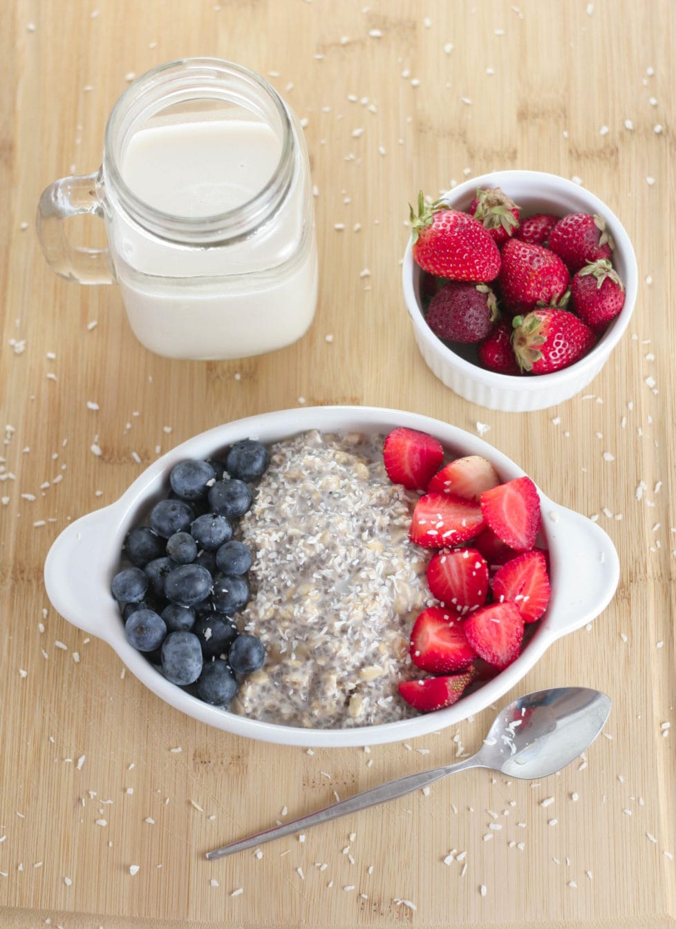 A bowl of overnight oats on a wooden table with berries and plant based milk