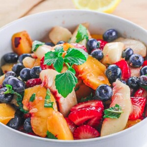 side view of fruit salad with basil in a white bowl