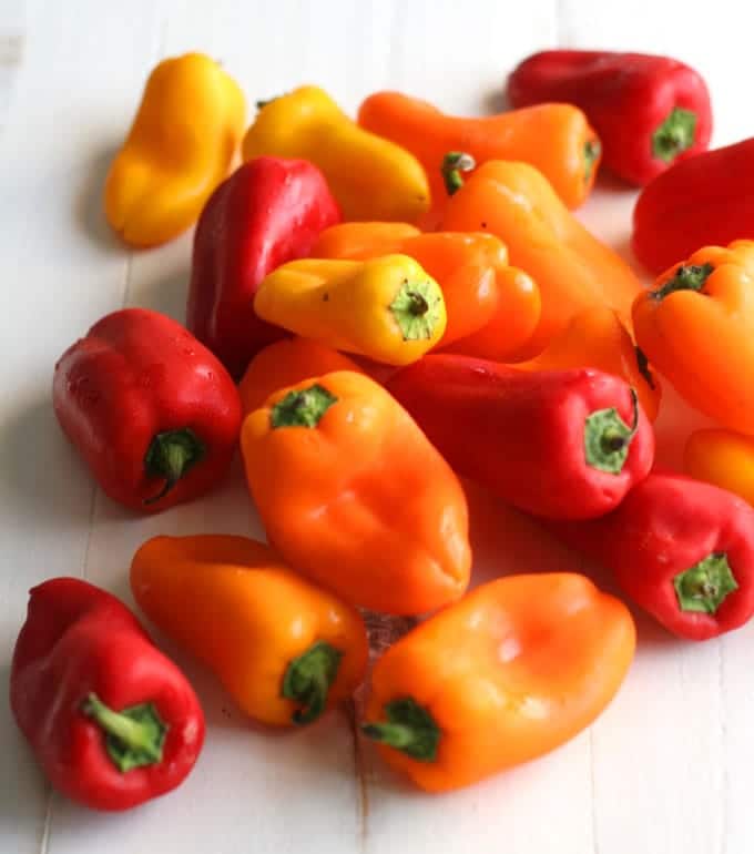 A bunch of different colored mini peppers on a white table