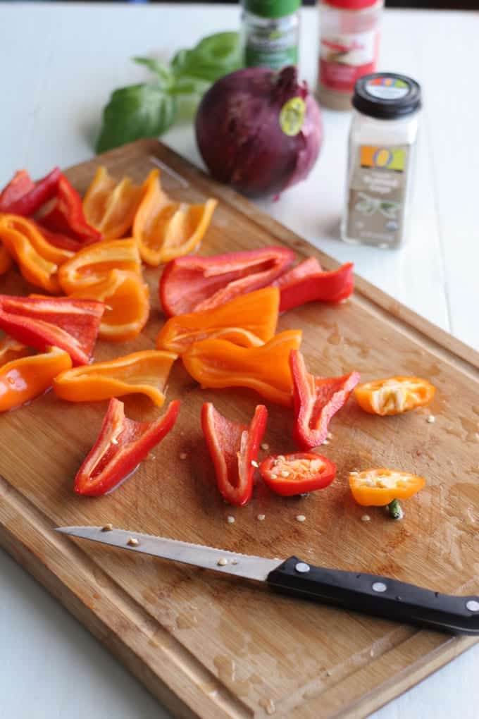 A knife sitting on top of a wooden cutting board, with Mini Peppers being sliced