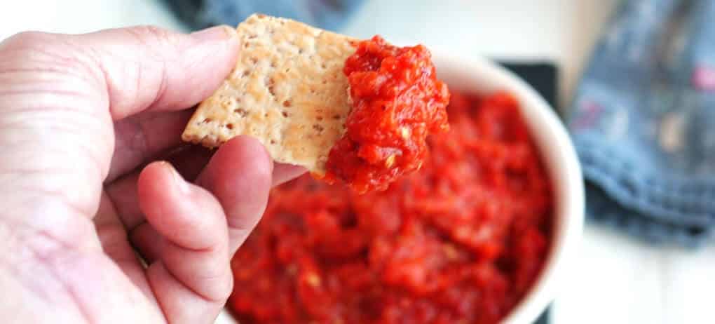 hand dipping cracker into red dip