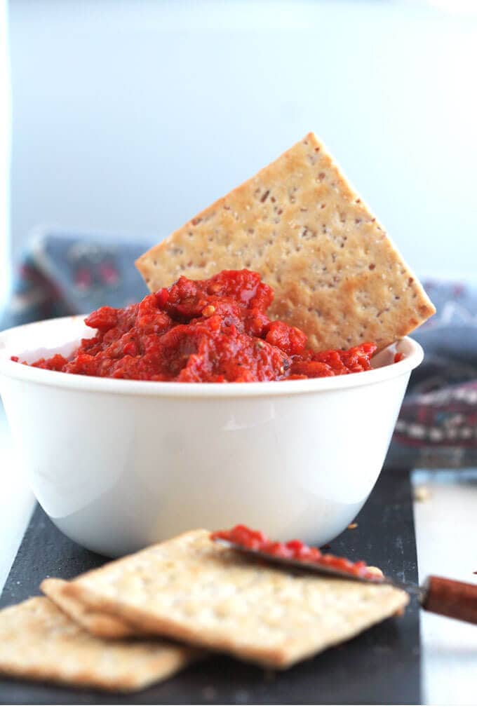 red dip in a white bowl with a cracker