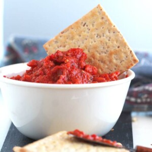 hot Serbian ajvar in a white bowl with a cracker in it.