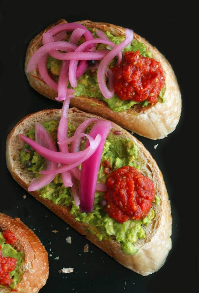two beautiful avocado tartines topped with pickled onions and hot ajvar