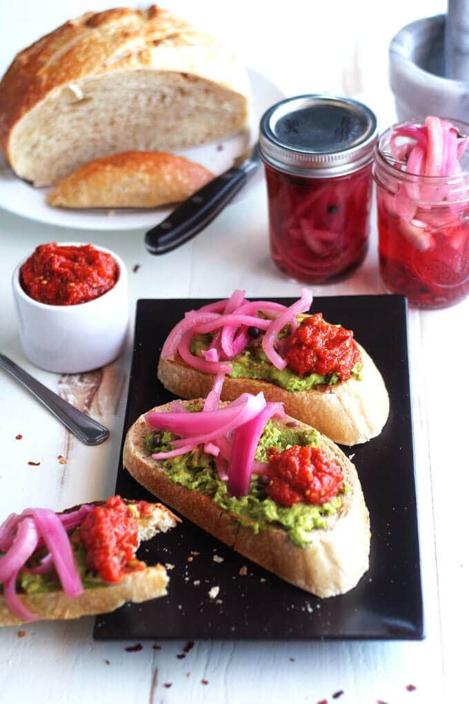 An overhead shot of avocado tartines on a black platter