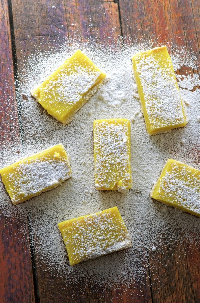 vegan lemon bars on a wood table sprinkled with powdered sugar