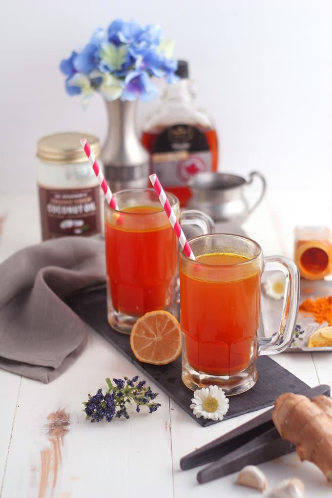 glasses of turmeric tonic surrounded by ingredients to make the recipe