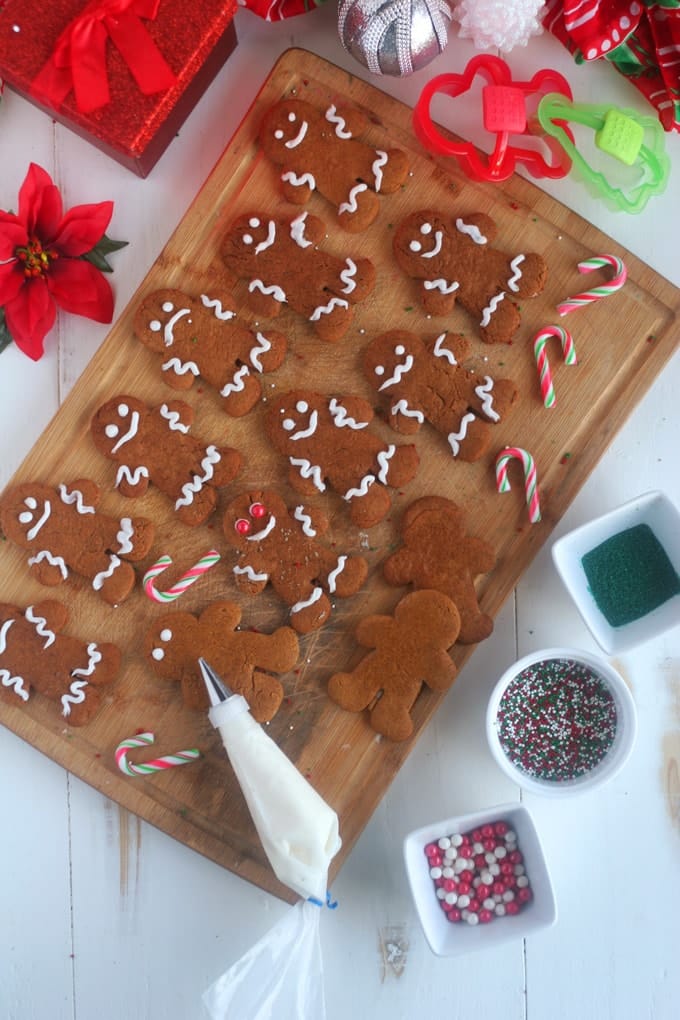 A cutting board with a bunch of gingerbread men on it with a person decorating one of them