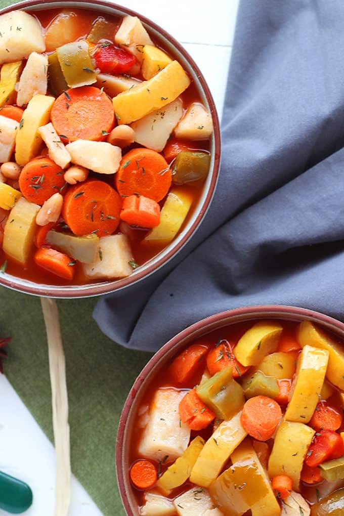 overhead view of bowl of vegan vegetable soup on a white wood table