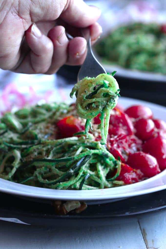 A close up of a person holding a forkful of pesto zoodles