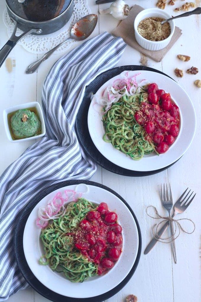 overhead shot of two white plates of zoodles on a white wooden table