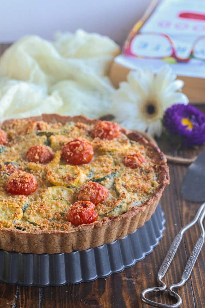 vegan tomato zucchini tart on a wooden table with flowers in background