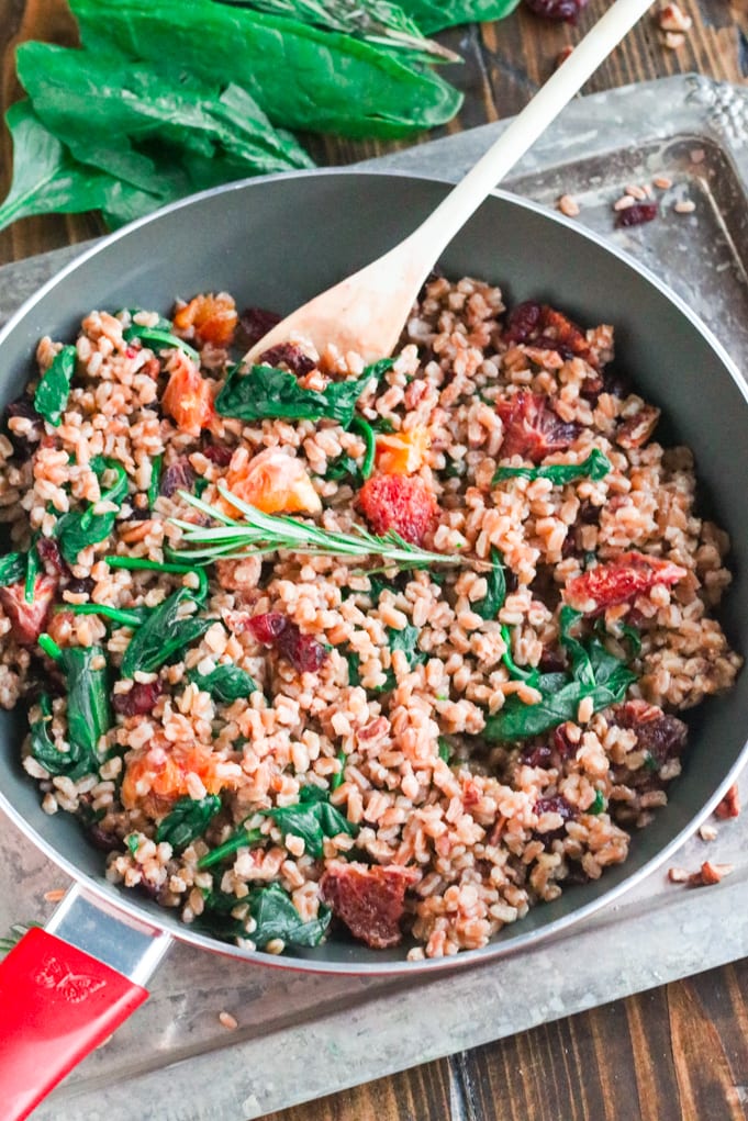 A skillet of Farro and Spinach with a spoon in it to stir