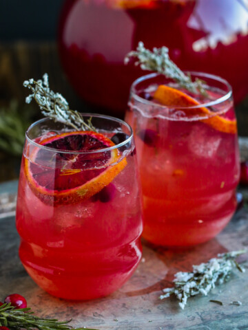 two glasses of cranberry spritzers on a table with candied rosemary