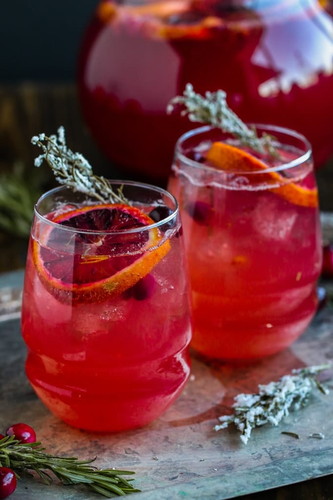 two glasses of cranberry spritzers on a table with candied rosemary 