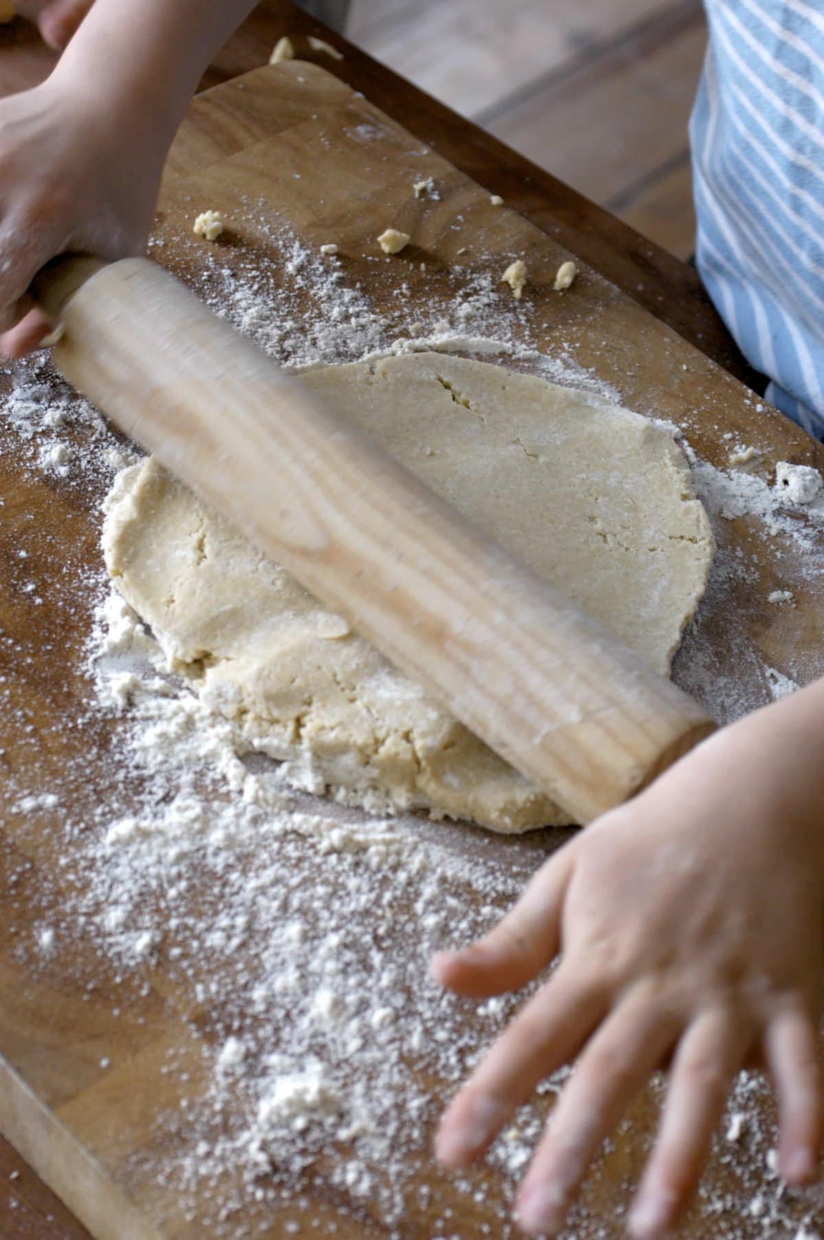 child rolling out vegan pot pie crust with a rolling pin on a wooden cutting board 