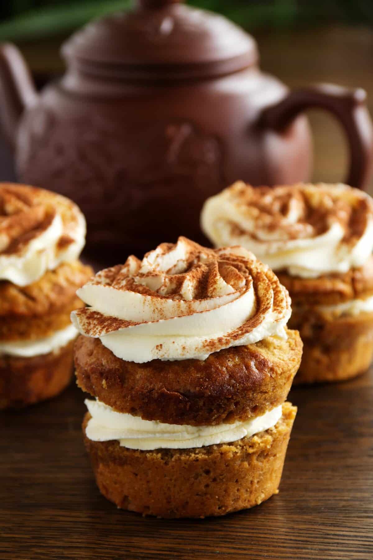 3 vegan sweet potato muffins sitting on top of a wooden table with a pot of tea in background