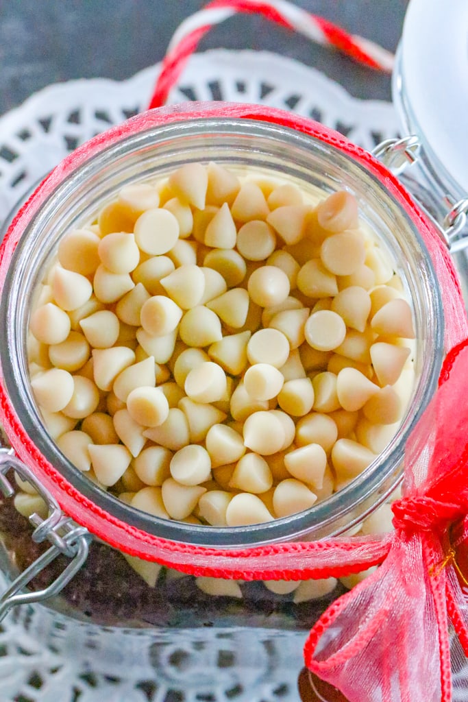 A jar of white chocolate chips and other ingredients for cookies