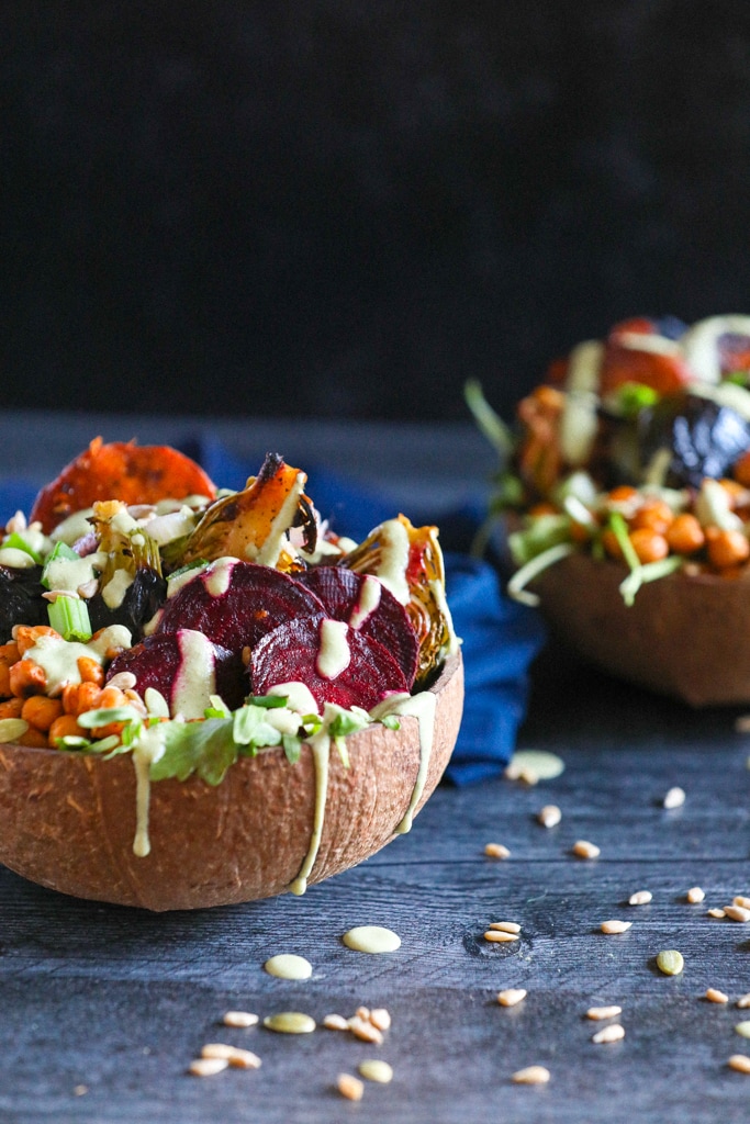 A side shot of roasted vegetables in a coconut bowl on a blue table
