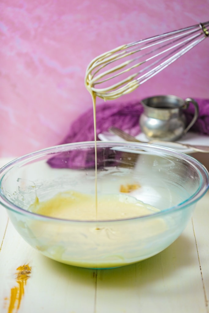 a whisk dripping batter over a clear bowl of pancake batter