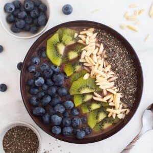 Acai smoothie bowl topped with fruit, seeds and nuts on a white table