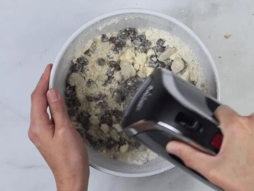 person using hand mixer to mix chocolate chips into cookie dough