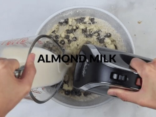 almond milk being poured into a bowl of chocolate chip cookie dough ingredients
