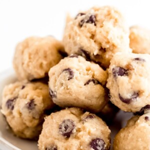 stack of cookie dough bites with chocolate chips on a white plate and sitting on a white table