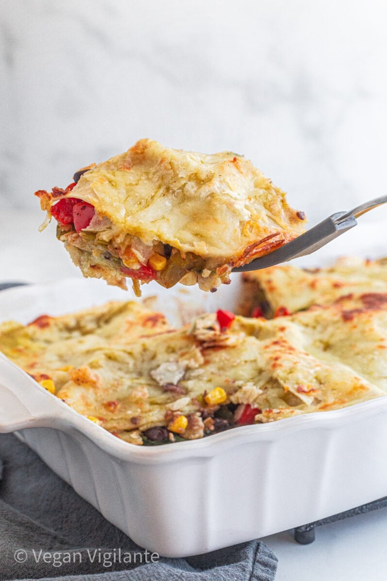 person scooping a slice of vegan enchilada casserole out of a white dish