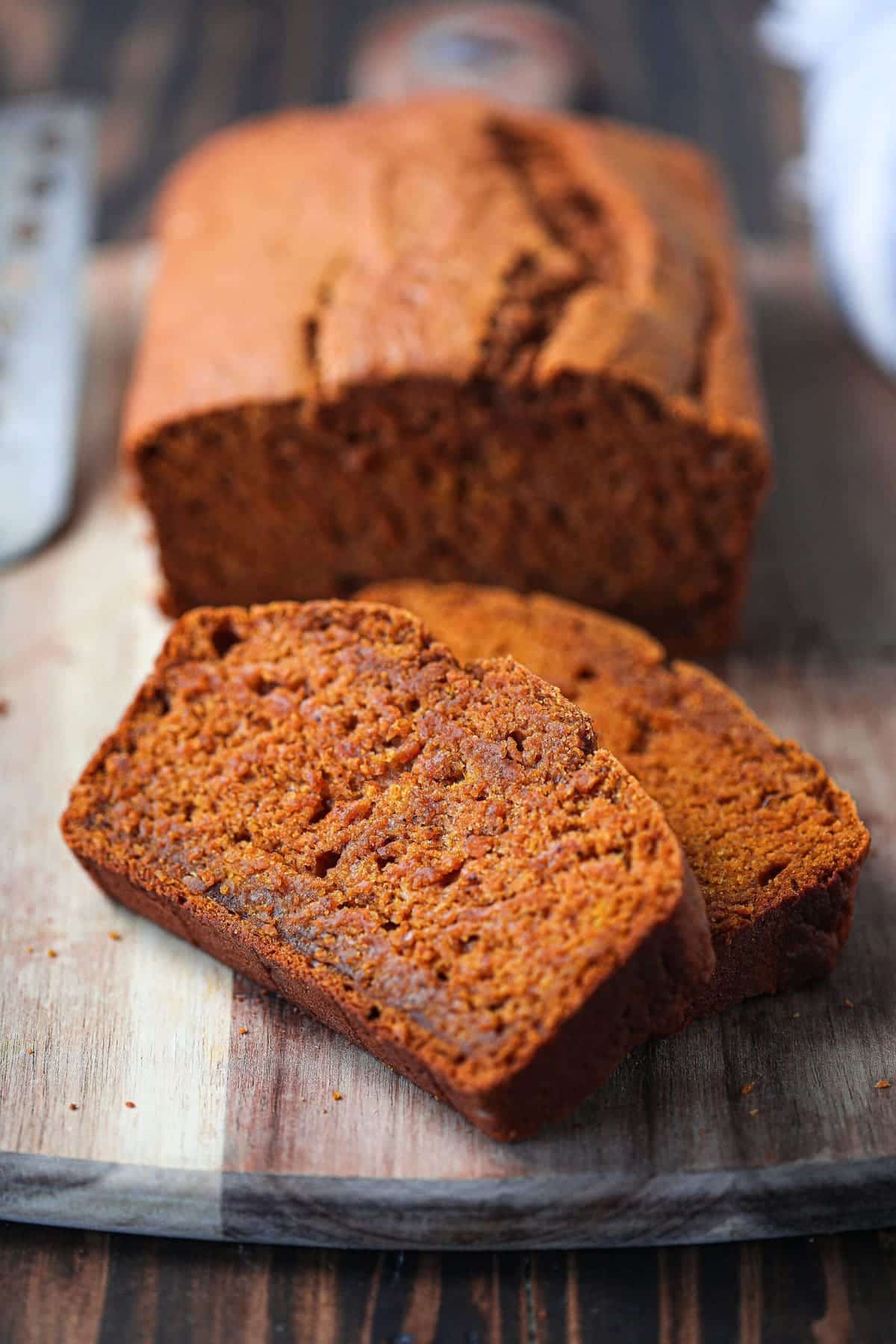 closeup shot of 2 slices of pumpkin bread on a wood cutting board with rest of loaf in background