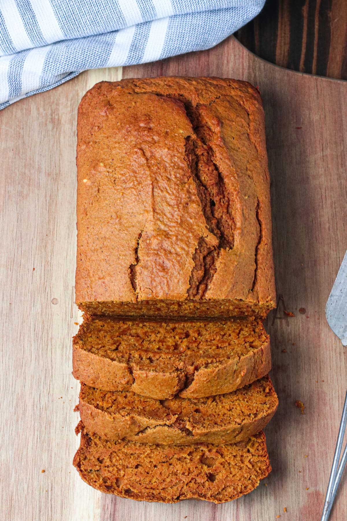 loaf of pumpkin bread on wooden cutting board with several slices cut