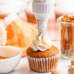 person frosting a pumpkin pie cupcake on a white table