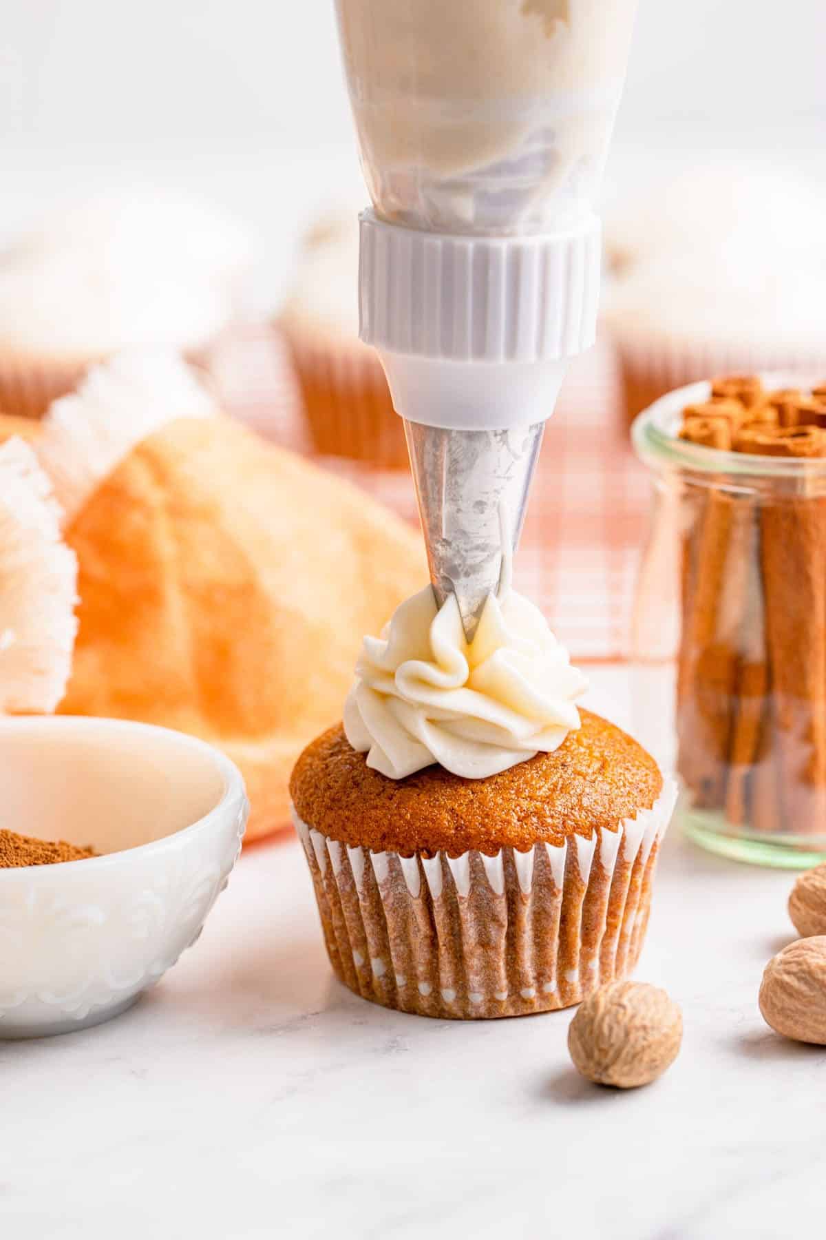 person frosting a pumpkin pie cupcake on a white table