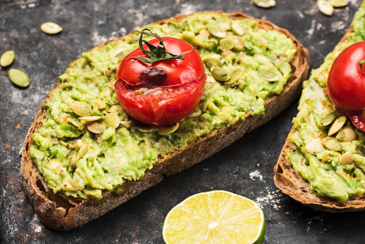 closeup of vegan avocado toast and tomato on a wooden table