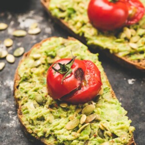 smashed avocado toast with roasted tomatoes and sunflower seeds on a table