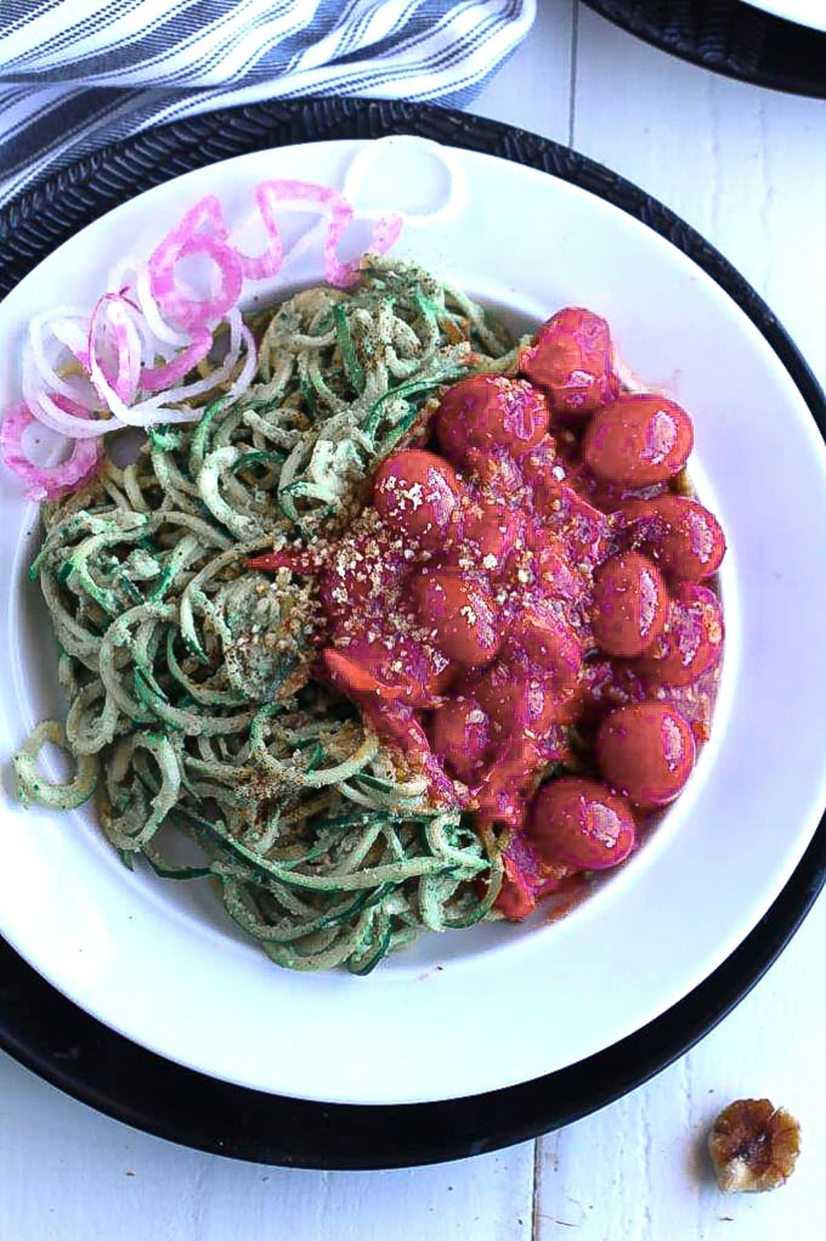 pesto zoodles on a white and black plate on a wood table