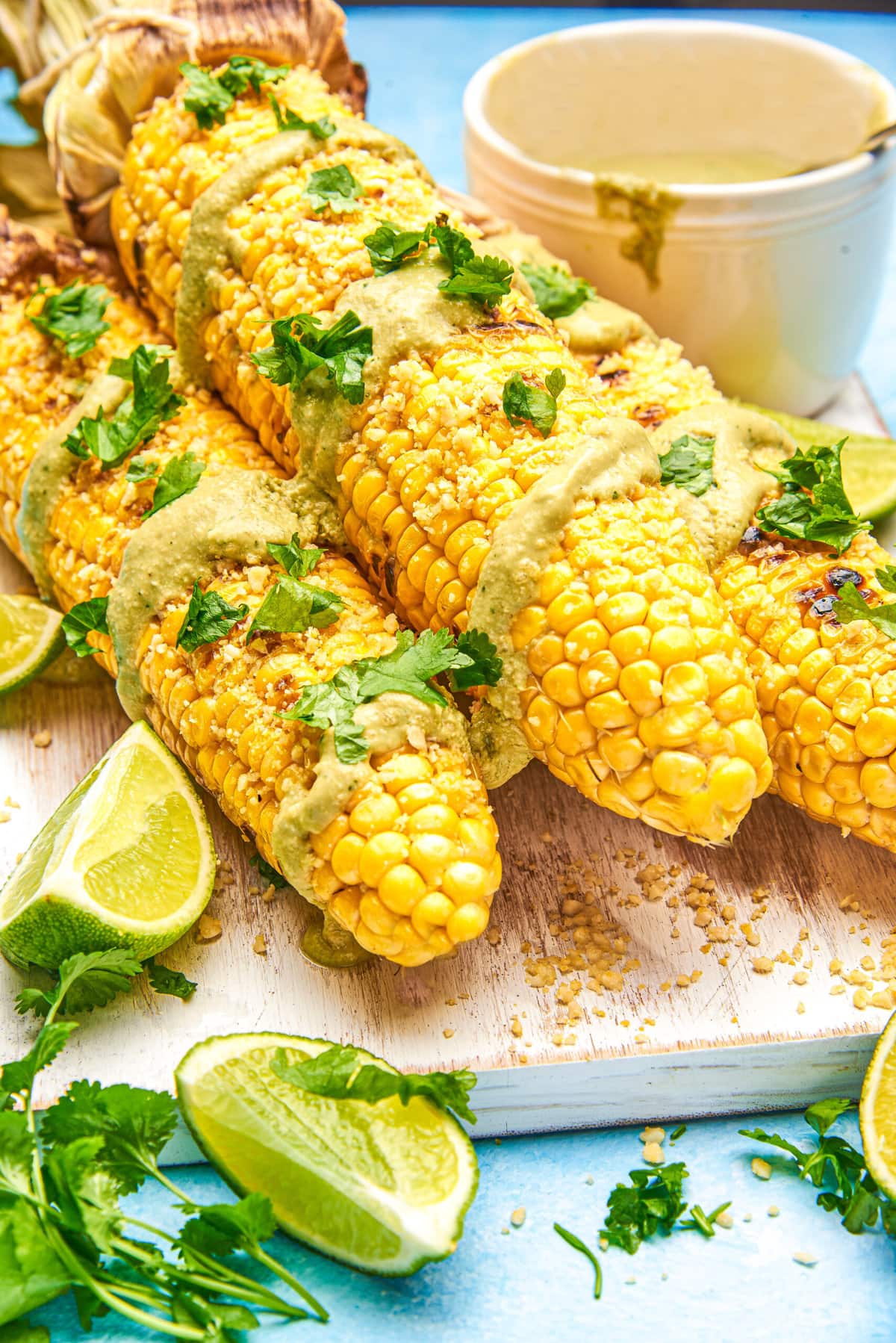 closeup of Vegan Street Corn grilled in the husk on a white cutting board and blue background. 