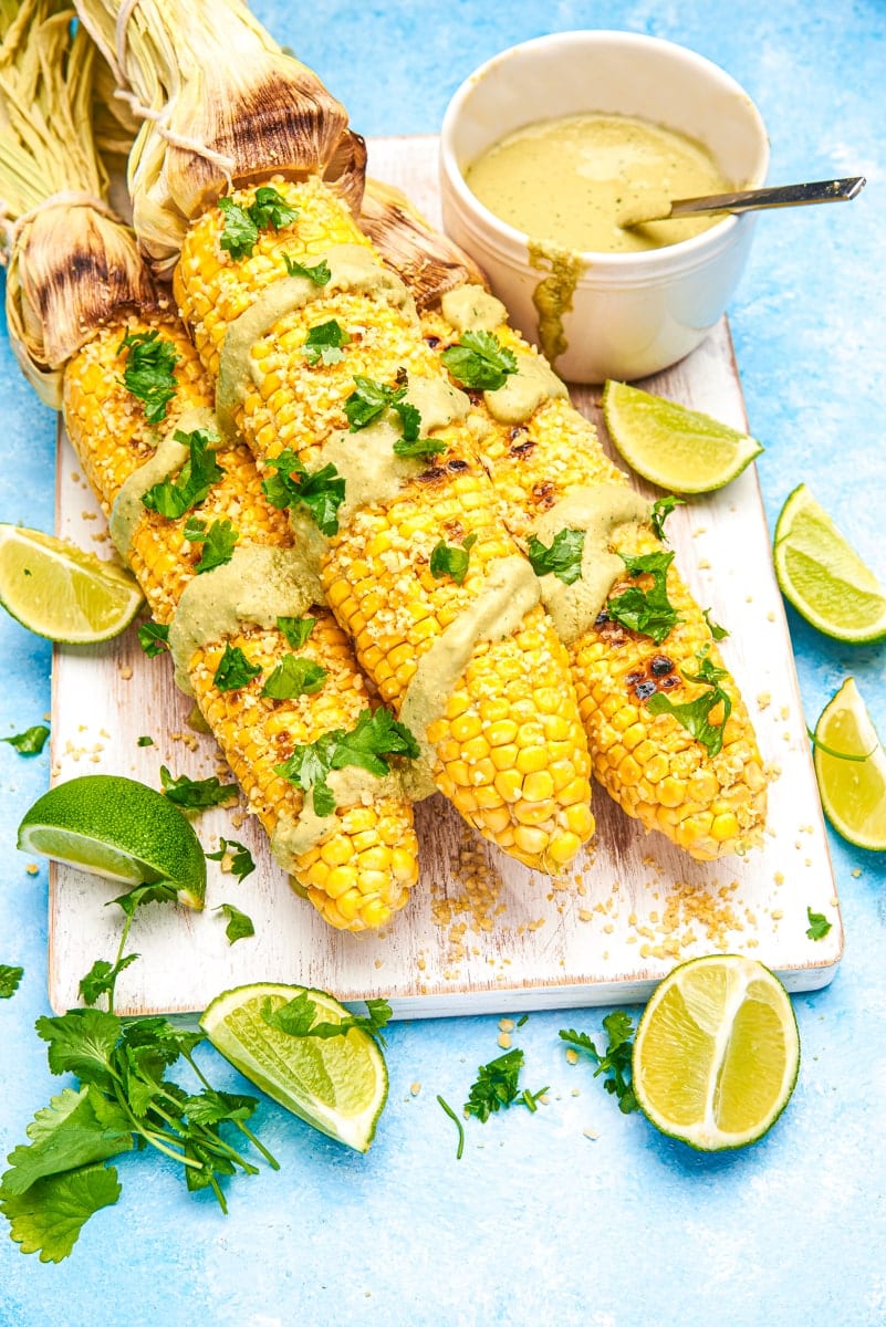 overhead view of Vegan Street Corn garnished with avocado sauce, cilantro and limes.