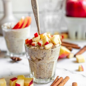 glass of apple pie overnight oats on white table with spoon in it