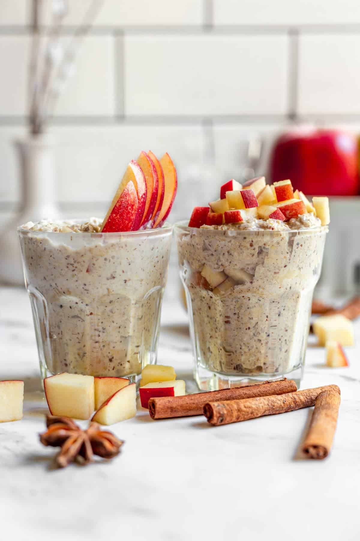 2 glasses of overnight oatmeal topped with apples on a white table