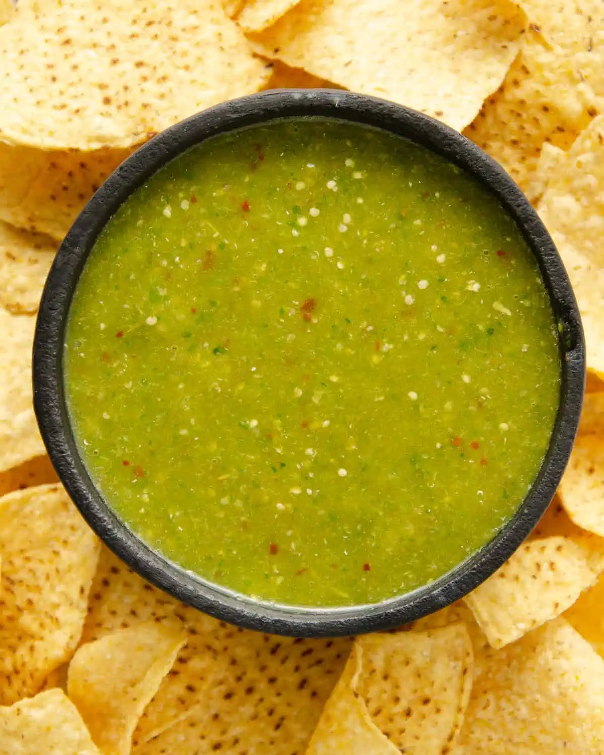 serrano salsa verde in a black bowl surrounded by chips
