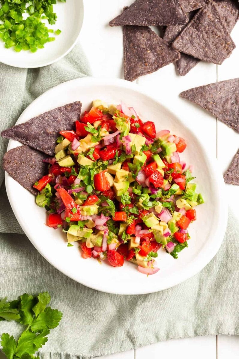 a bowl of strawberry avocado salsa on a white wood table