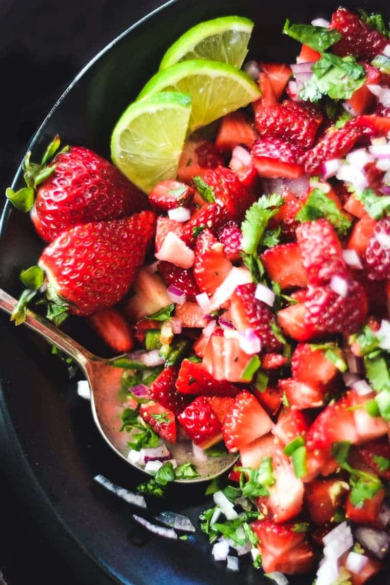 strawberry jalapeño salsa in a dark bowl garnished with green leaves