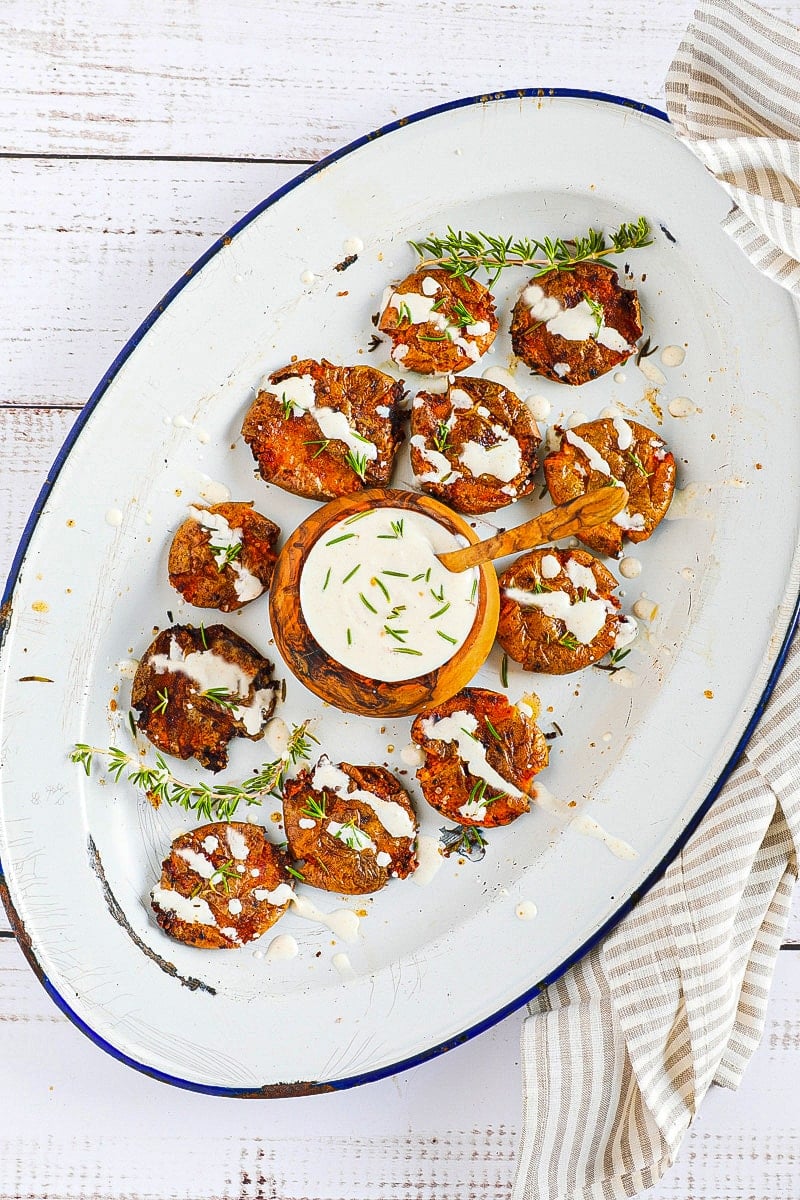 white plate with air fryer smashed potatoes drizzled with garlic aioli on a wooden table