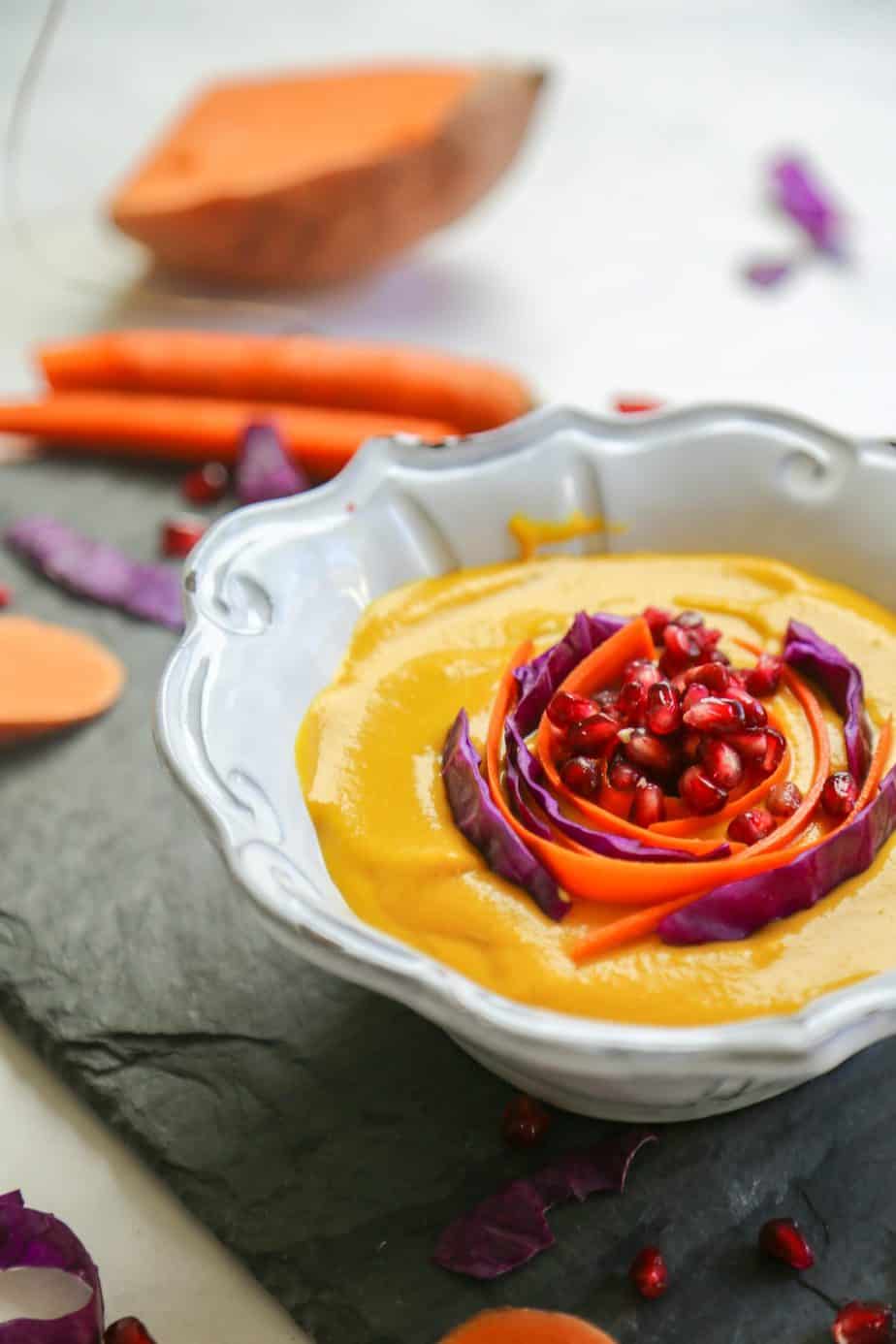 a bowl of bright yellow soup topped with purple cabbage, carrots and pomegranate seeds