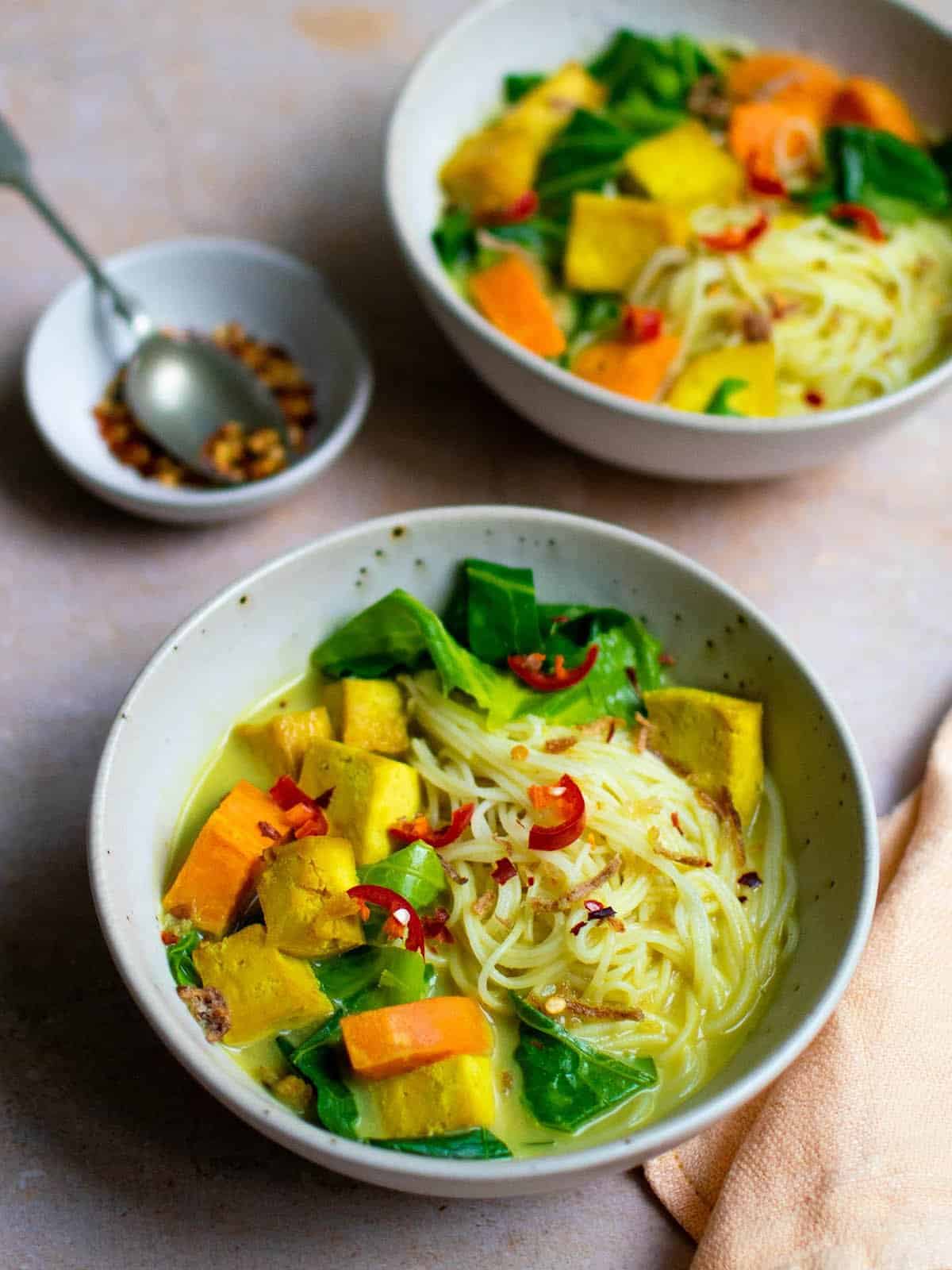 2 bowls of colorful Thai soup on a table