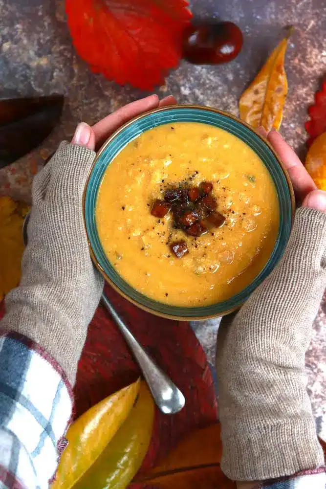 2 hands holding a bowl of yellow soup topped with meatless ham