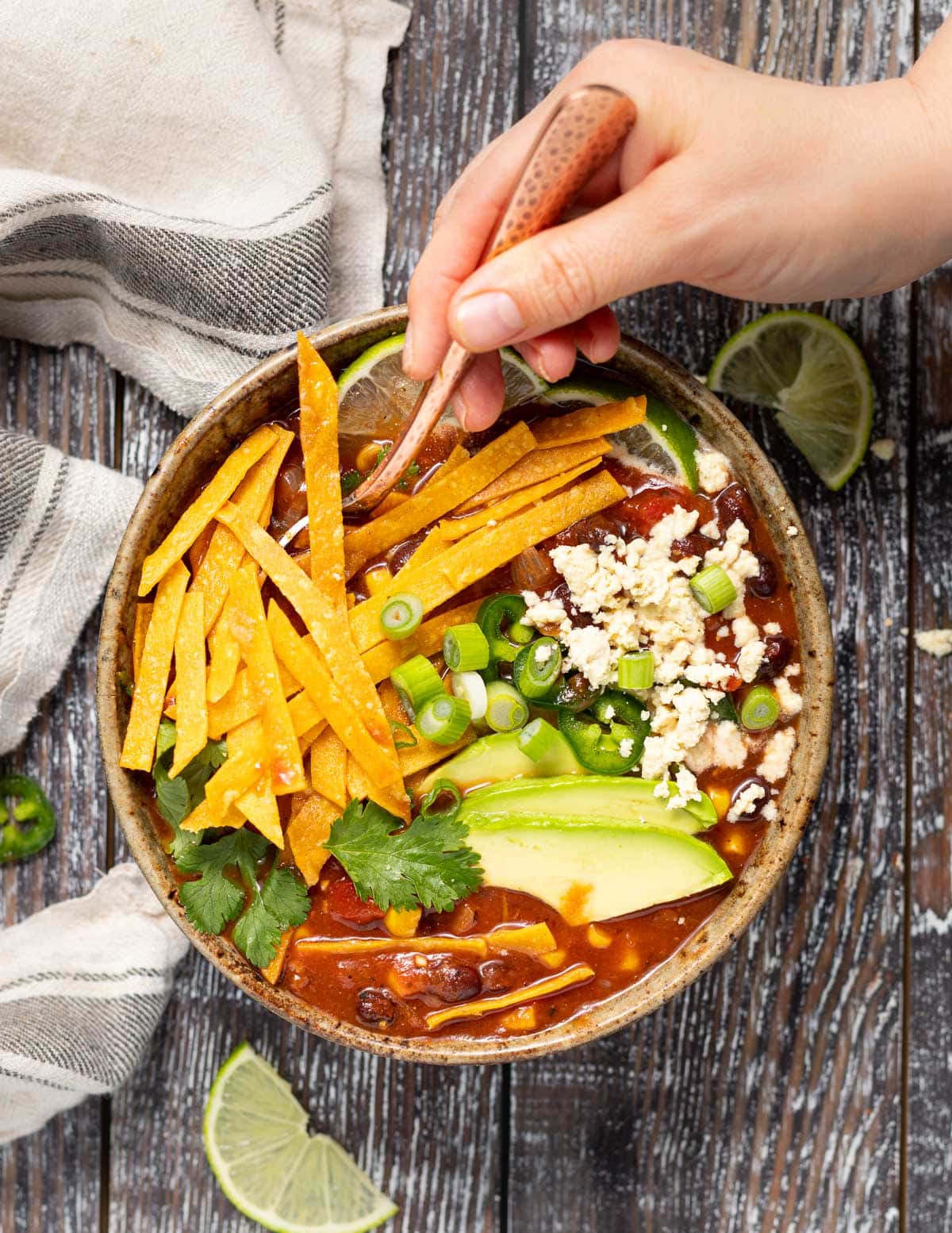 a hand dipping a spoon into a bowl of vegan tortilla soup