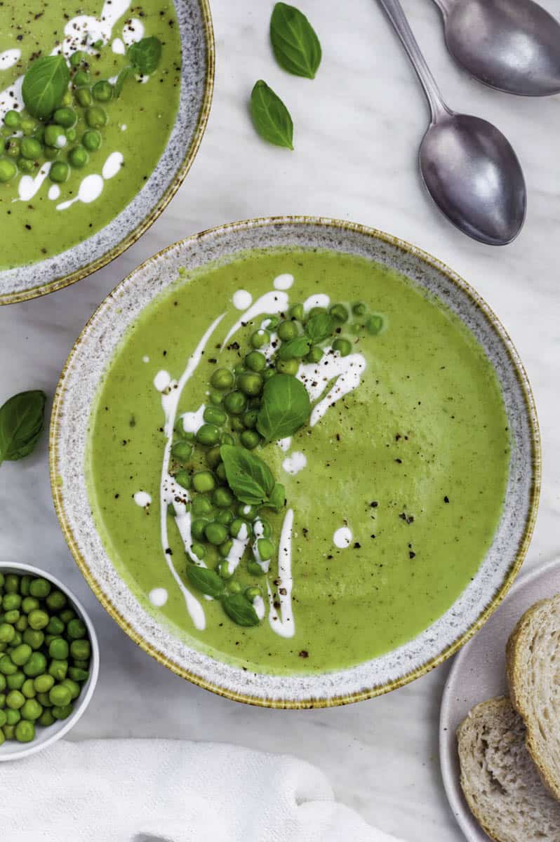 2 bowls of green soup on a white tablecloth topped with peas